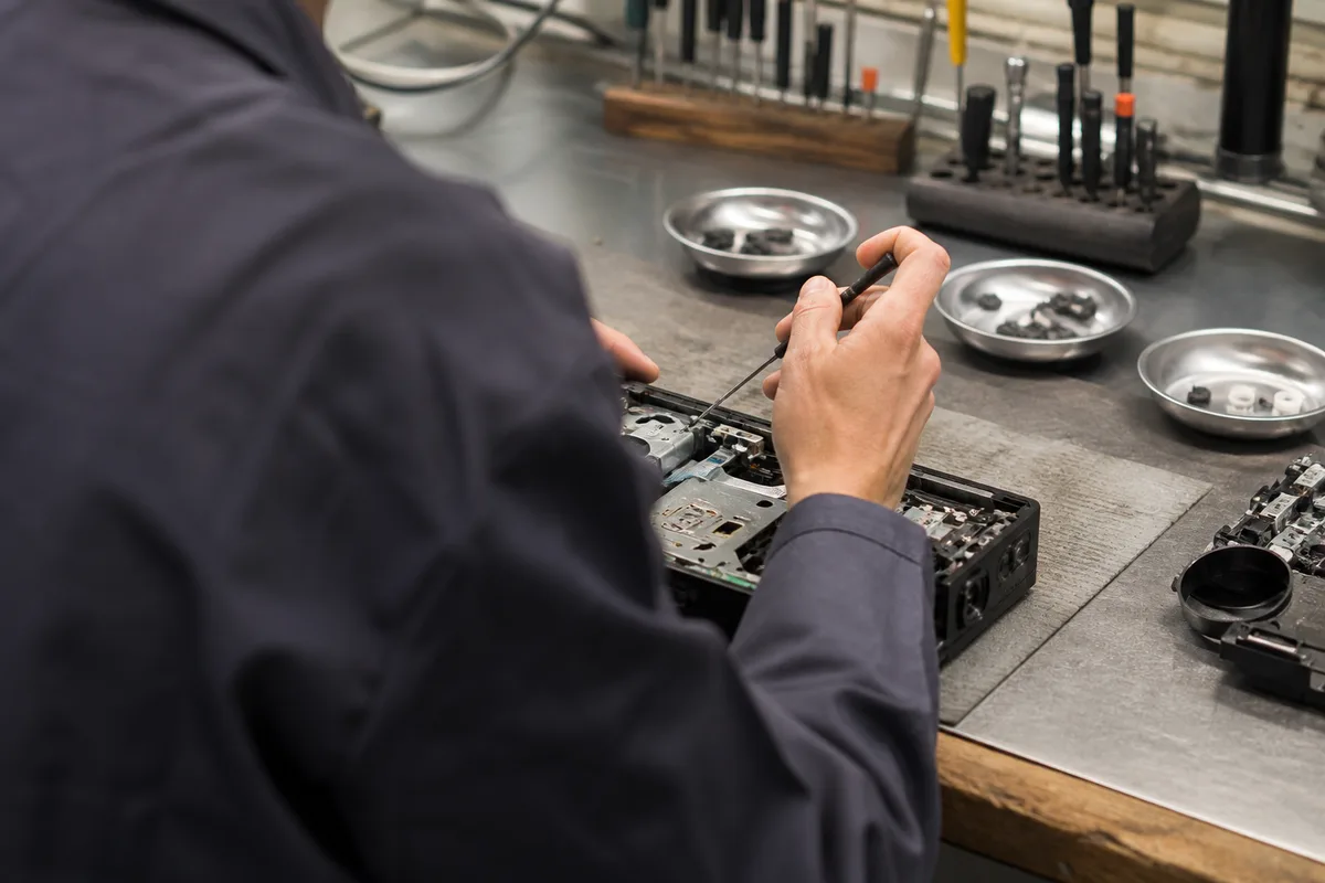 Atelier de réparation lumineux, mains d’un technicien tenant un tournevis au-dessus d’un capot ouvert